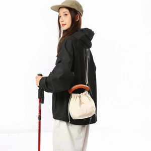 Detail view of cream canvas drawstring tote bag with orange handle and black windbreaker