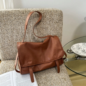 Detail of vintage brown soft leather messenger bag on a woven chair in a cozy setting