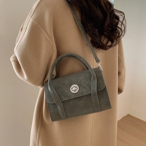 Olive green crossbody bag shown on a model wearing a camel wool coat in a stylish setting