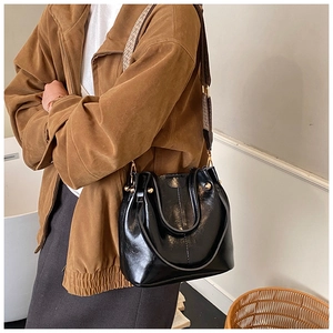 Detail of glossy black bucket bag with a stylish patterned wide woven shoulder strap