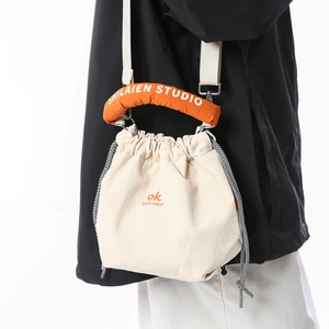 Detail view of cream drawstring bucket bag with vibrant orange padded handles and brand logo