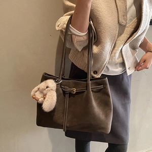 Detail of dark brown suede tote bag with metal buckle and plush bunny charm pendant