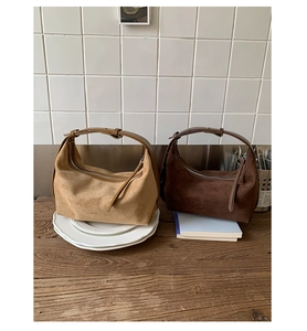 Détail rapproché de sacs hobo en daim kaki et marron foncé sur une surface en bois naturel