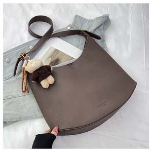 Détail d'un sac demi-lune en cuir marron foncé avec pendentif ours sur veste en jean