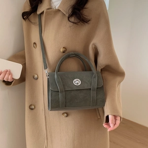Close-up of dark green leather shoulder bag with silver twist-lock and camel coat contrast