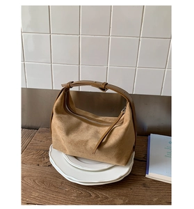 Detailed view of camel suede crescent bag on white plates with a vintage wood background