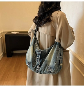 Detail of washed denim hobo bag with silver studs worn by a model in beige coat