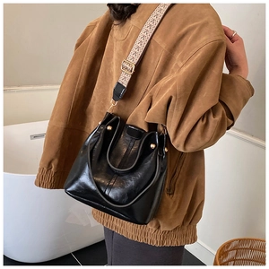 Detail der schwarzen glänzenden Beuteltasche mit Boho-Gurt und goldenen Nieten am Model