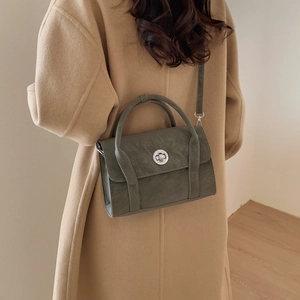 Detail of a dark green crossbody bag with a metal twist lock on a wool coat