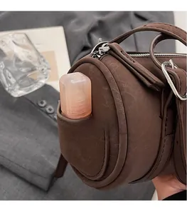 Detail view of brown cylinder bag side pocket showing cosmetic bottle storage capacity