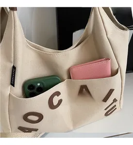 Detail of canvas tote bag showing side pocket, leather letter patch, and interior capacity
