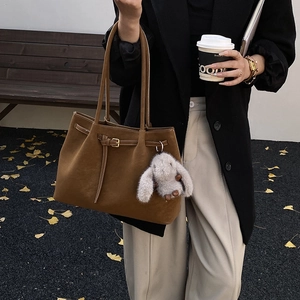 Deep brown matte suede tote bag with plush bunny charm in a stylish commute setting