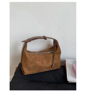 Détail du sac dumpling en daim marron avec bandoulière réglable sur fond minimaliste
