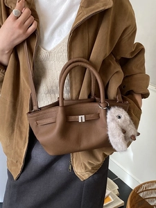 Brown leather bucket bag with silver buckle and plush charm, worn by model in brown jacket