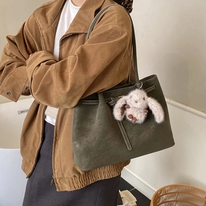 Detail view of dark green tote bag with contrast stitching and plush bunny charm
