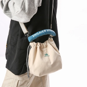 Detail view of a beige drawstring bucket bag with blue shoulder strap on a model