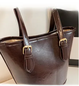 Close-up of brown glossy PU leather tote bag with adjustable gold buckles and straps