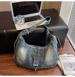 Detail of vintage washed denim hobo bag with metallic rivets on a desk setting