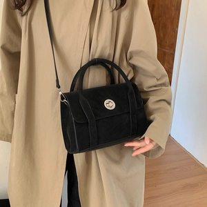 Detail of a black matte crossbody bag featuring a silver round turn-lock and dual handles