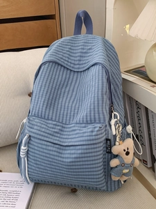 Blue plaid school backpack with cute bear pendant on a minimalist beige sofa