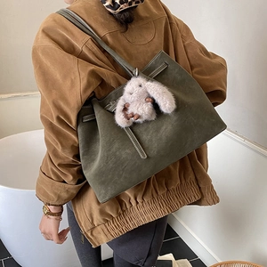 Detail of dark green suede tote bag featuring a cute white rabbit plush keychain