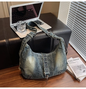Detailed view of washed denim hobo bag with silver studs on a desk with laptop