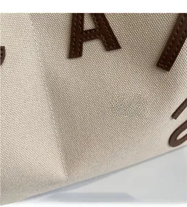 Detailed close-up of beige canvas fabric texture with dark brown leather letter patches