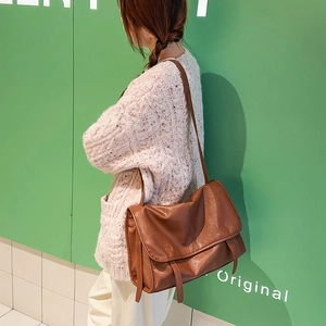 Close-up of brown vintage messenger bag with flap closure on green wall background