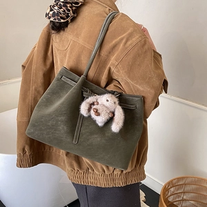 Detailed side view of an olive green matte tote bag with a grey plush bunny pendant