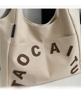 Close-up of beige canvas tote bag with brown 3D TAOCAITU lettering and woven label