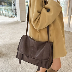Close-up detail of a vintage dark brown leather satchel bag with wide flap and vertical stitching