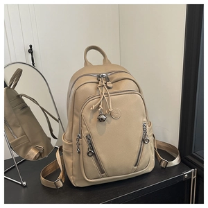 Detailed macro view of beige lychee leather backpack with metal bell charm on dark surface