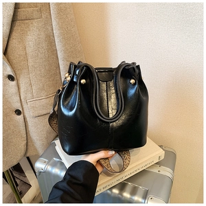 Detail of black glossy leather bucket bag with gold spherical buckle and animal print strap