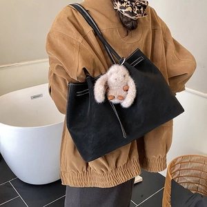 Detail of black suede tote bag featuring white contrast stitching and a rabbit charm