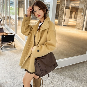 Close-up of a brown leather messenger bag styled with a yellow wool coat in street fashion