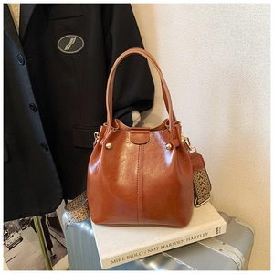 Detail of vintage caramel bucket bag with ethnic woven strap on a silver suitcase