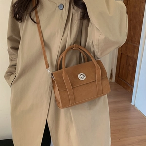 Detailed view of a vintage brown crossbody bag with silver round twist lock on a trench coat
