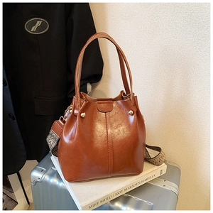 Close-up of brown oiled leather bucket bag with metal studs and patterned strap