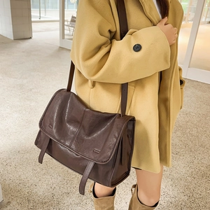 Brown vintage messenger bag carried by a model in a long coat in a modern setting