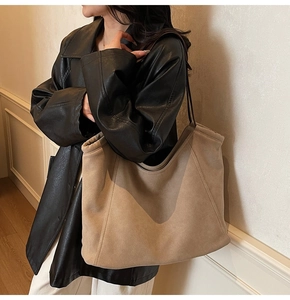 Detail of a khaki suede tote bag with brown straps worn on a black leather jacket