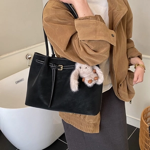 Detail of black suede tote bag featuring white contrast stitching and a plush rabbit charm