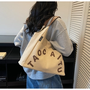 Detail of beige canvas tote bag featuring brown leather letter patches and logo tag