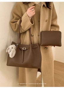 Brown litchi grain tote bag set with a plush bunny charm on a model in wool coat