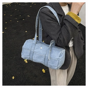 Detail of light blue denim cylinder shoulder bag with silver buckle flap pocket