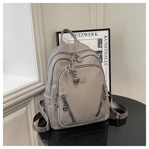 Detail of grey lychee leather backpack with metal logo, zip pockets and tassel charm