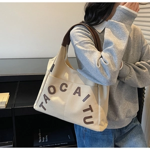 Close-up of beige canvas tote bag with leather straps and 3D letter embroidery detail