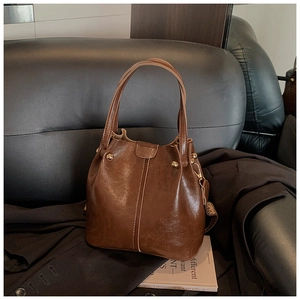 Detail of vintage brown bucket bag with smooth leather texture and gold hardware on sofa