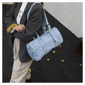 Close-up of a light blue denim barrel bag with metal rivets and wide adjustable strap