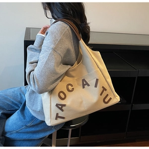 Close-up of canvas tote bag with brown leather handles and 3D letter embroidery