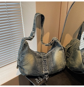 Detailed view of washed blue denim shoulder bag featuring silver rivets and metal ring